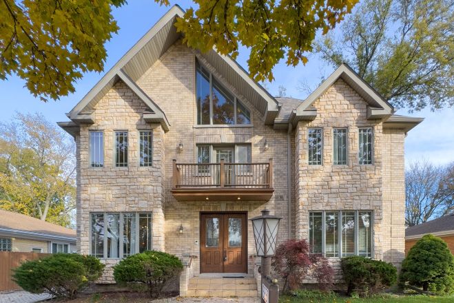 Elegant brick house with a lush garden and driveway, under a clear sky.