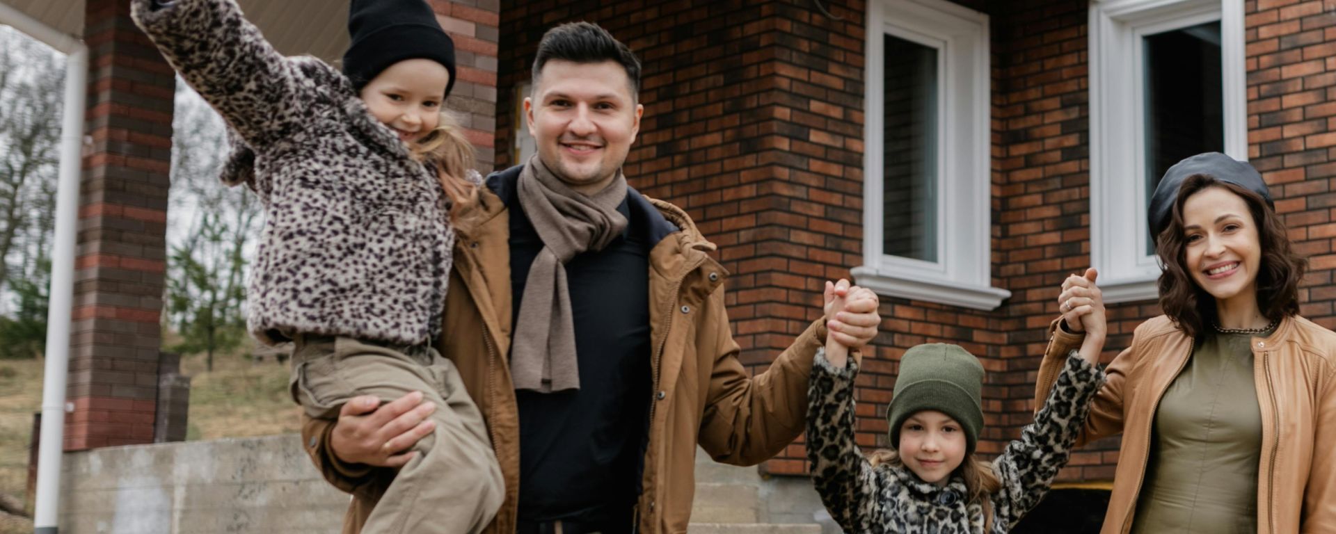 Joyful family celebrates new home purchase with smiles and warm attire.