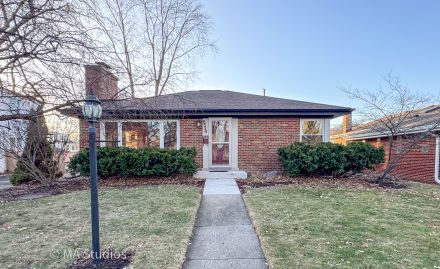 Elegant brick house with a lush garden and driveway, under a clear sky.