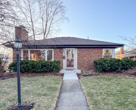Elegant brick house with a lush garden and driveway, under a clear sky.