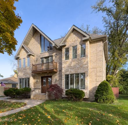 Elegant brick house with a lush garden and driveway, under a clear sky.