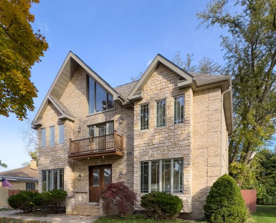 Elegant brick house with a lush garden and driveway, under a clear sky.
